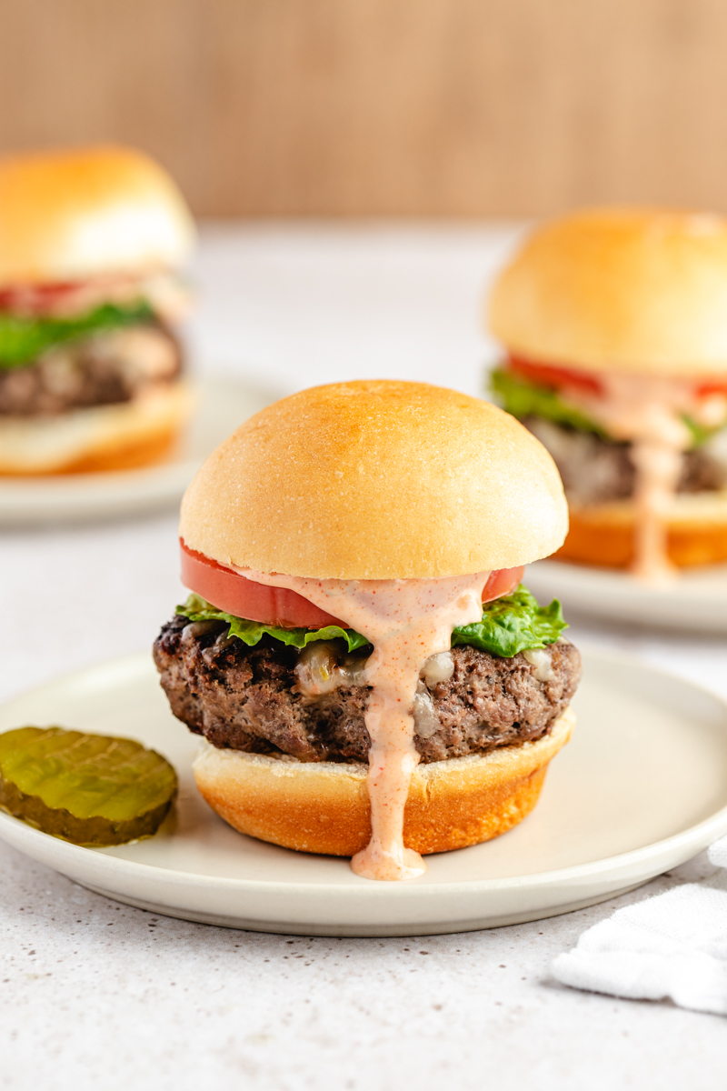 A hand-smashed slider with melted cheese, lettuce, tomato and house sauce on a soft bun